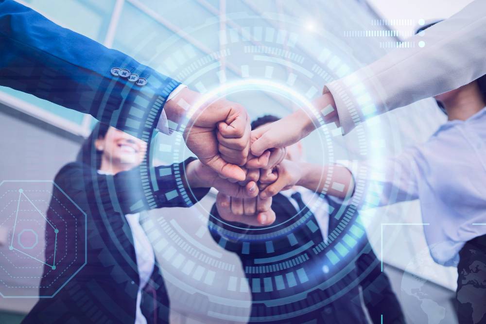 A group of business professionals stacking hands in a gesture of teamwork and unity, with a futuristic digital interface overlay suggesting technology or data-driven collaboration.” This description emphasizes concepts related to business networking, teamwork, and corporate challenges.